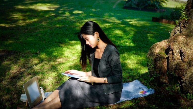 Vrouw leest een e-reader in het zonlicht onder een boom
