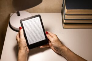 Handen houden een e-reader met tekst naast een stapel boeken vast